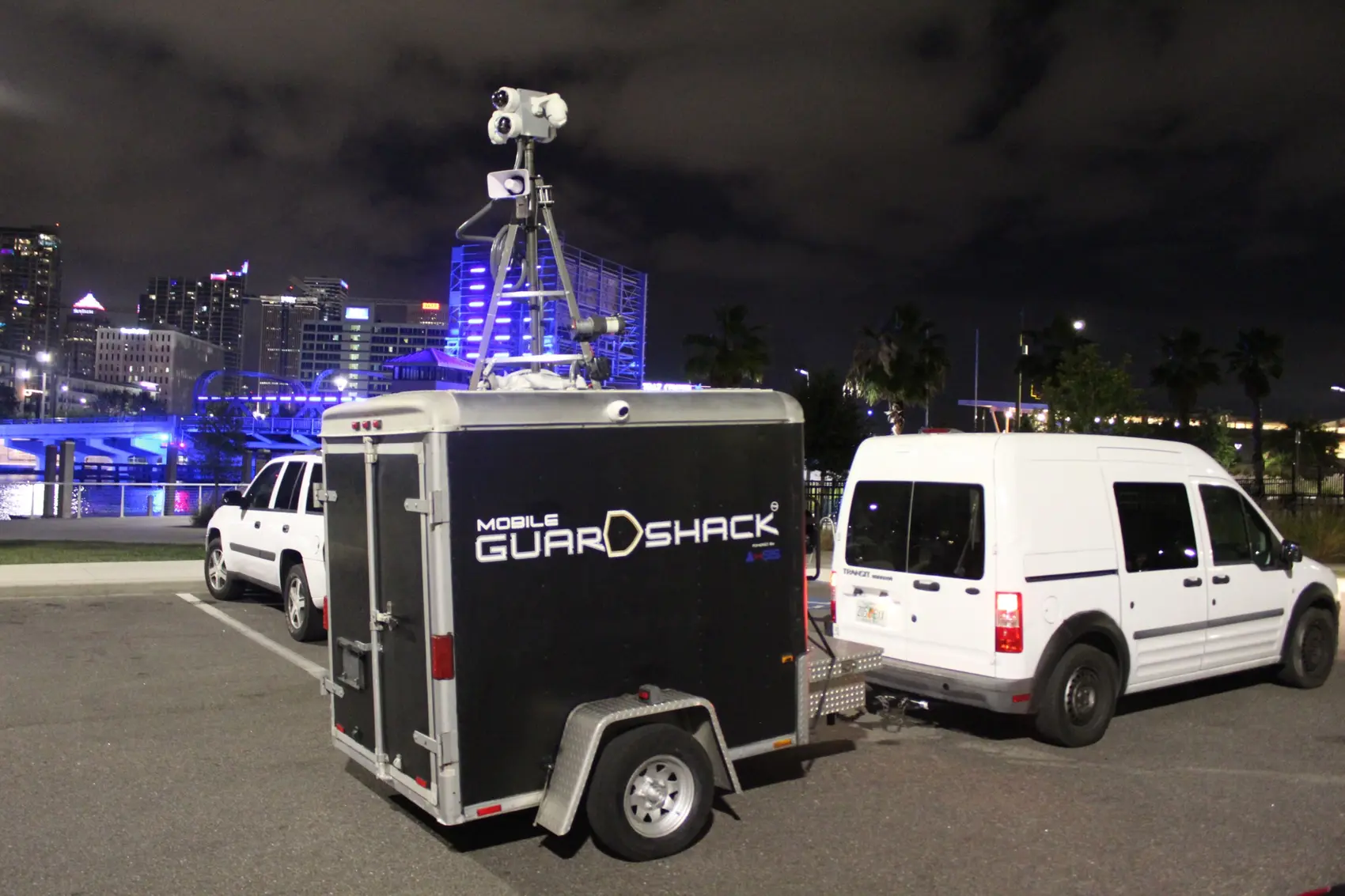 Real Mobile GuardShack side view operating at night with branded black trailer, single axle and elevated multi-camera mast